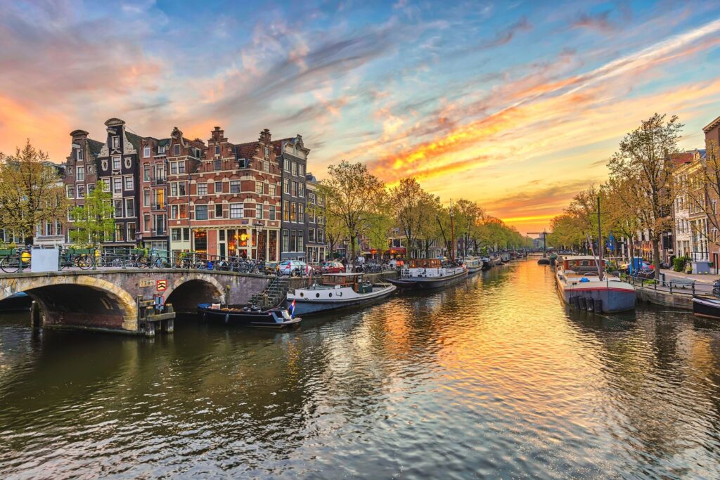 Grachten in Amsterdam tijdens zonsondergang met historische woningen en boten op het water, iconisch beeld van Nederland, toeristische bestemming, mooie zonlicht reflectie, stadsleven en grachtenpanden.