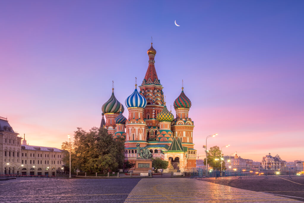 Rustig uitzicht op het kleurrijke Sint Basiliusplein in Moskou tijdens zonsopgang met een heldere hemel en de maan in de achtergrond, perfect voor reisinspiratie en cultuur.