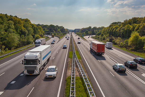 - Moderne snelweg met vrachtwagens en auto's in Nederland, omringd door groene natuur en helder weer.