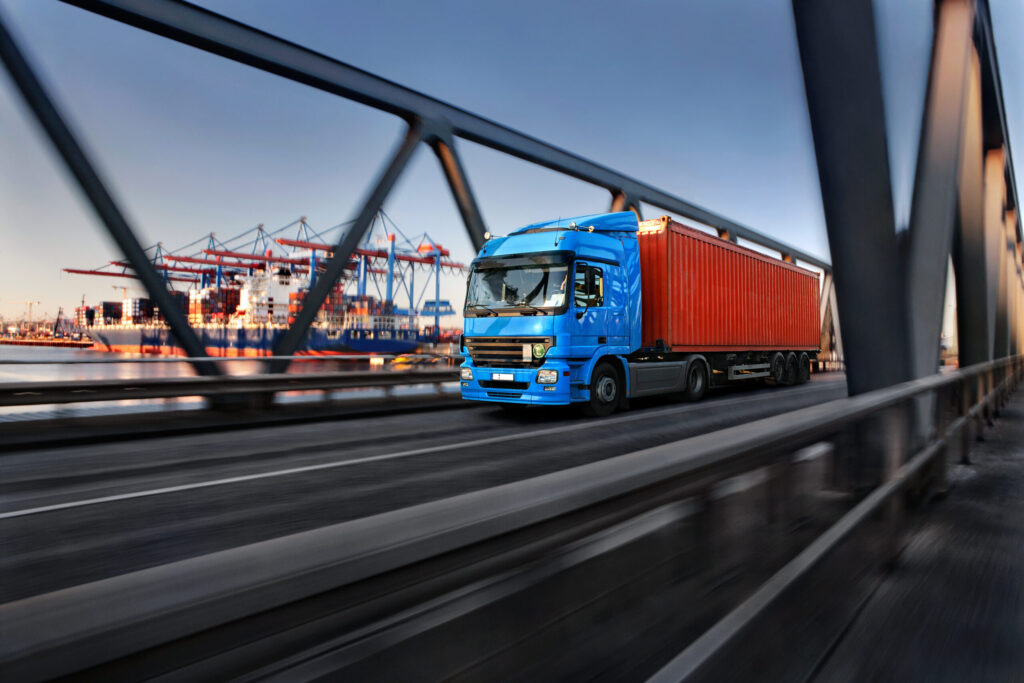 Container vrachtwagen op brug met haven en containers op achtergrond, logistiek en transport, wegtransport, containervervoer en supply chain activities.