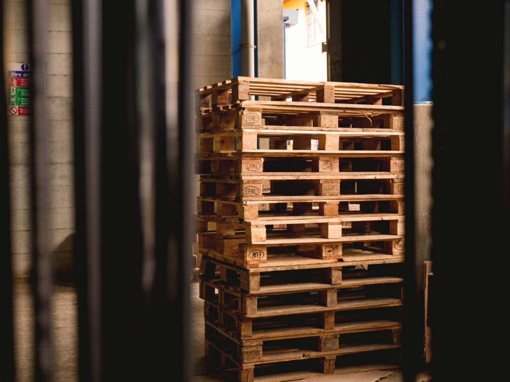 Etenswaardige pallets gestapeld in een magazijn, klaar voor verzending of opslag, met een achtergrond van industriële omgeving en natuurlijke lichtinval.