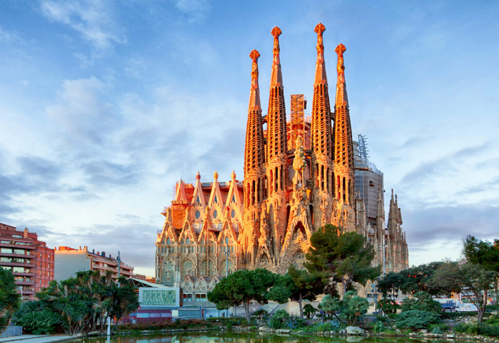 Prachtige foto van de Sagrada Família in Barcelona verlicht door de zonsondergang, met een heldere blauwe hemel en groene bomen op de voorgrond voor een indrukwekkend architectuurbeeld.