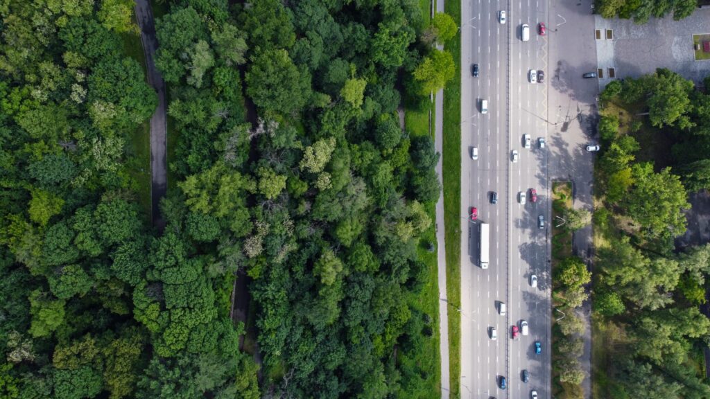 Groene bosrand en drukke stadsweg met auto’s en trucks vanuit vogelperspectief, natuur en verkeer in balans met focus op logistiek, transport, en duurzame mobiliteit.
